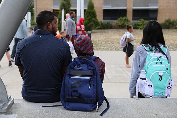 一个成年人和一个学生坐在学校外面.