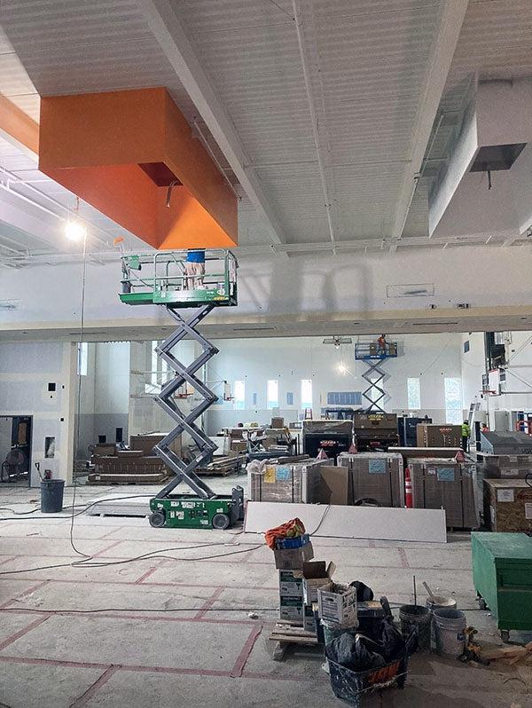 一个大的开放式室内空间有剪刀式升降机，工人们在天花板固定装置的区域作画