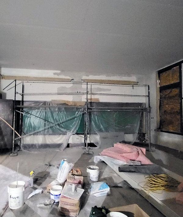 一间大房间正在建造中，窗户用刨花板填充, scaffolding, and plastic; buckets, 粉色绝缘球棒, 其他的建筑材料在房间的中间