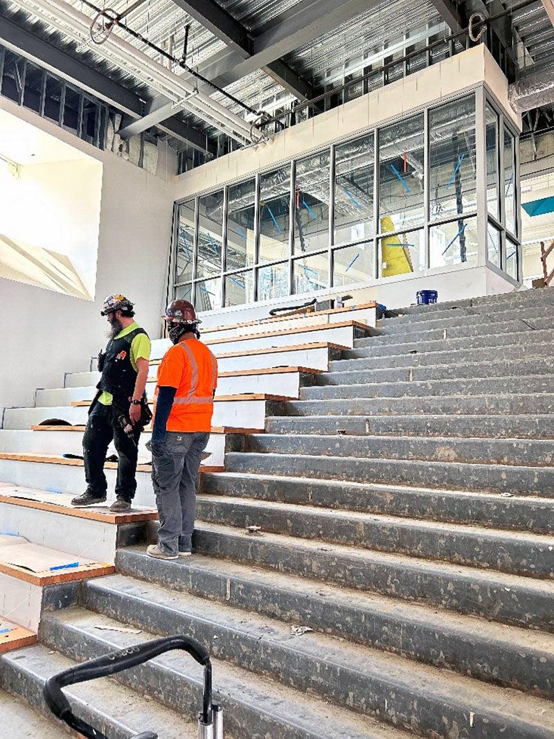一个工人站在混凝土楼梯上，另一个站在两倍高的木楼梯上