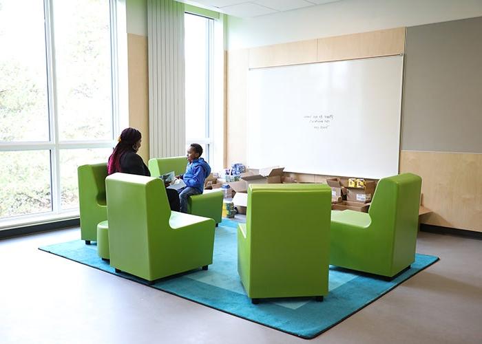 一组石灰绿色的椅子摆放在角落里的绿松石地毯上，两边都有窗户. 一个成人和一个儿童站点在两个座位上